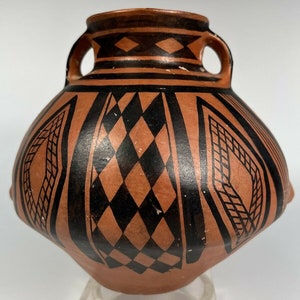 May include: A brown ceramic pot with two handles and black geometric designs. The pot has a rounded body and a slightly flared rim.