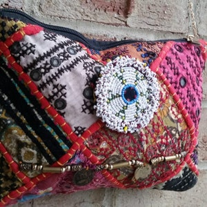 May include: A colorful patchwork fabric purse with a beaded circle design and a zipper closure. The purse has a chain strap and is made of various fabrics in shades of red, pink, black, and white.
