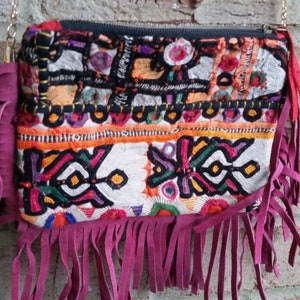 May include: A small, colorful patchwork purse with a long, fringed strap. The purse is made of different fabrics and has a variety of embroidery details. The fringe is a deep burgundy color.