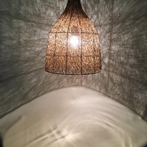 May include: A woven brown pendant light fixture hangs from the ceiling, casting a warm glow on the white surface below.
