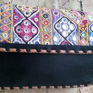 May include: A black leather clutch purse with a colorful embroidered flap featuring mirrored accents. The flap has a geometric pattern with yellow, blue, pink, and green embroidery.
