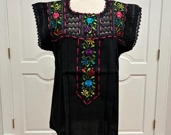 May include: Black embroidered cotton blouse with colorful floral designs and lace trim around the neckline and sleeves.