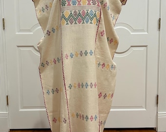 May include: A white cotton dress with colorful embroidered geometric patterns. The dress has a loose fit and a round neckline. The embroidery is in shades of red, green, blue, yellow, and pink.