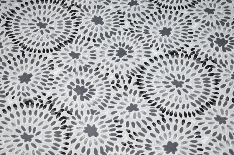 K&ouml;nnte beinhalten: Ein wei&szlig;er Stoff mit einem sich wiederholenden Muster aus schwarzen und grauen stilisierten Blumen. Die Blumen bestehen aus kleinen, ovalen Formen, die von einem zentralen Punkt nach au&szlig;en strahlen.