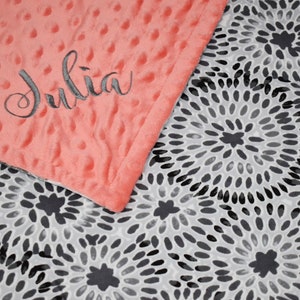 K&ouml;nnte beinhalten: Eine korallenrosa Minky-Babydecke mit einem schwarzen und wei&szlig;en Wirbelmuster auf der R&uuml;ckseite. Die Decke ist mit dem Namen "Julia" bestickt, der in grauer Farbe gestickt ist.