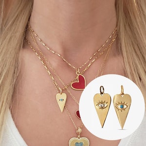 May include: A gold necklace with three layered chains and four heart-shaped pendants. The pendants are a red heart, a gold heart with a blue evil eye, a gold heart with a white evil eye, and a gold heart with blue and white crystals.
