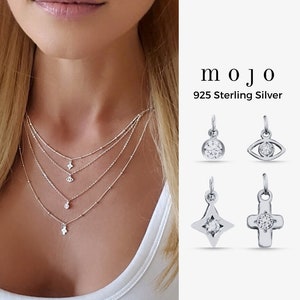 May include: A silver necklace with multiple strands and a variety of charms, including a star, a cross, an eye, and a circle. The charms are all set with small, clear stones. The necklace is made of 925 sterling silver. mojo 925 Sterling Silver
