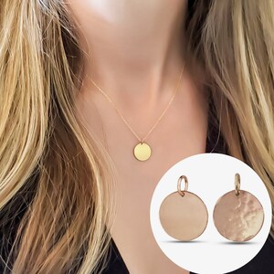May include: A gold-colored necklace with a round pendant is displayed. The pendant hangs from a delicate chain. Two additional round pendants are shown, one with a hammered texture, and one smooth.