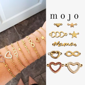Könnte beinhalten: Goldfarbene Armbänder mit Herz-, Unendlichkeits- und Sternanhängern werden an einem Handgelenk gezeigt. Zusätzliche goldene Anhänger mit Herz-, Stern-, Unendlichkeits- und Knoten-Designs werden gezeigt. Das Wort "mojo" ist in Schwarz gedruckt.