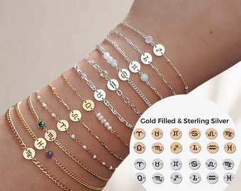 May include: A set of 12 gold filled and sterling silver zodiac sign charm bracelets. Each bracelet features a different zodiac sign charm and a small gemstone bead. The charms are arranged in a row on a white background. Gold Filled & Sterling Silver.
