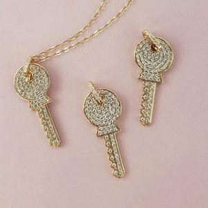 May include: Three gold key necklaces with clear crystal accents. The necklaces are on a pink background with the text "talk is chic" in gold lettering.