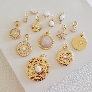 Puede incluir: Una colección de dijes dorados con piedras de ópalo y diseños de estrella. Los dijes están dispuestos sobre una superficie blanca.