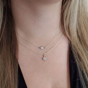 May include: A layered necklace set featuring a dainty chain with a small oval opal connector and a cable chain with a star-shaped pendant. The text in the image reads: Styles top to bottom: Kaylani dainty chain, Liva connector, Cali cable necklace, Raina star pendant.