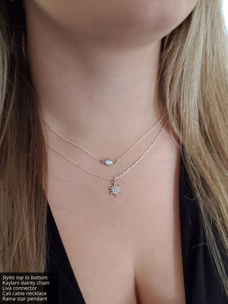 May include: A layered necklace set featuring a dainty chain with a small oval opal connector and a cable chain with a star-shaped pendant. The text in the image reads: Styles top to bottom: Kaylani dainty chain, Liva connector, Cali cable necklace, Raina star pendant.