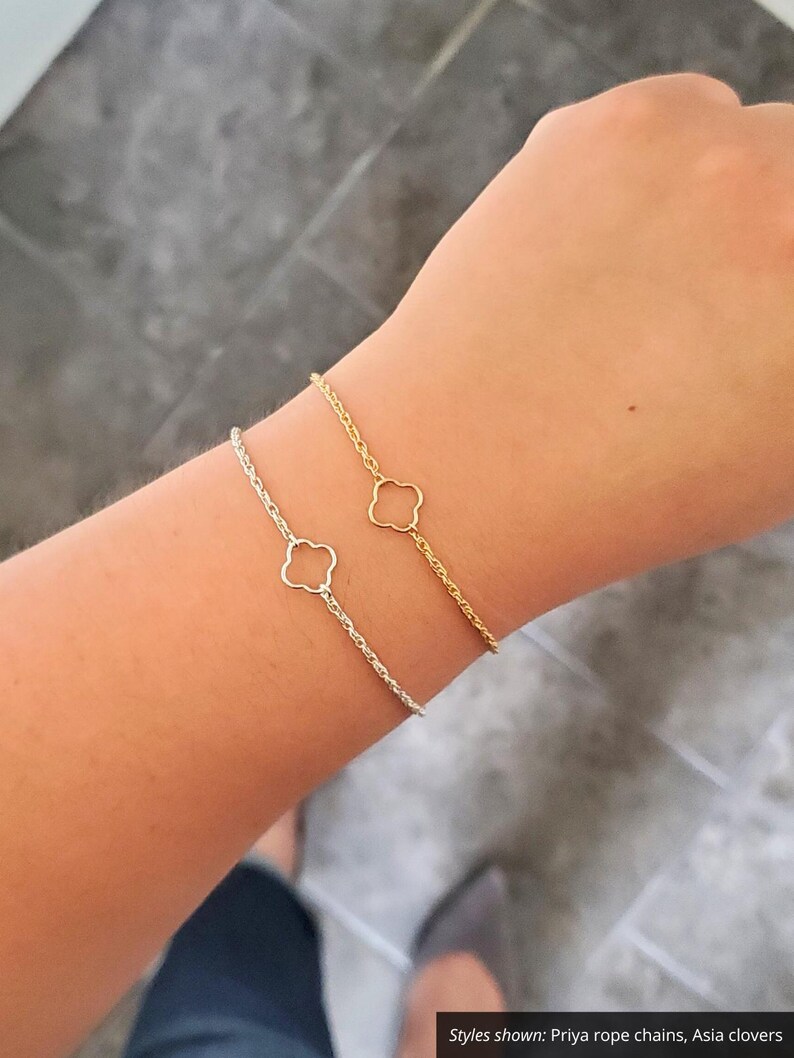 May include: Two delicate bracelets on a wrist. One is a gold rope chain with a four-leaf clover charm, the other is a silver rope chain with a four-leaf clover charm.  Styles shown: Priya rope chains, Asia clovers.
