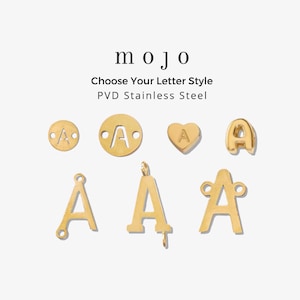 May include: A collection of gold-colored PVD stainless steel letter A charms in various shapes, including circular, heart-shaped, and stylized letter forms. The text "mojo Choose Your Letter Style PVD Stainless Steel" is displayed above the charms.