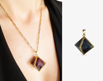 May include: A gold chain necklace featuring a geometric pendant with a faceted, dark purple and blue stone encased in a gold metal frame. The pendant is shaped like a double pyramid, suspended from a delicate gold link chain with a polished finish.