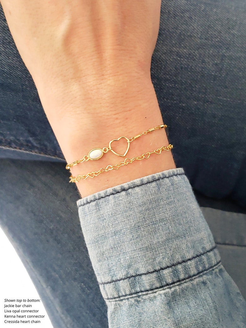 May include: A gold heart charm bracelet with a white opal connector. The bracelet is layered with two chains, one with a heart design and the other with a bar design.