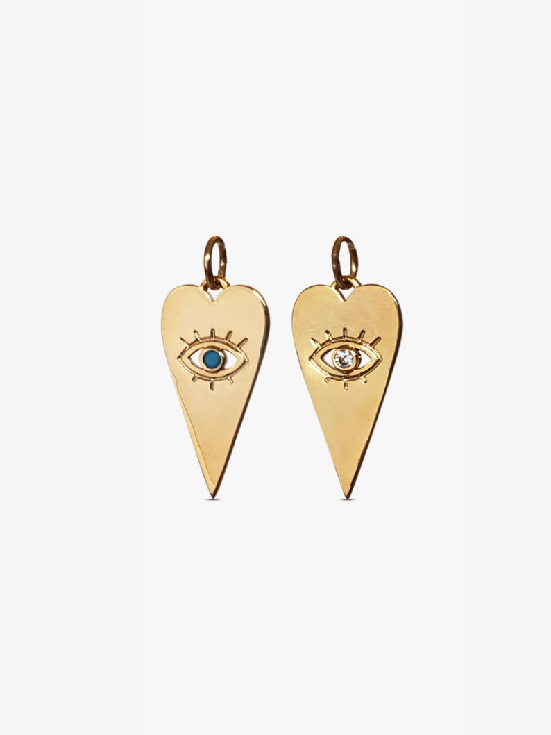 May include: Two gold heart-shaped pendants with an evil eye design. One pendant has a blue stone in the eye, and the other has a clear stone.