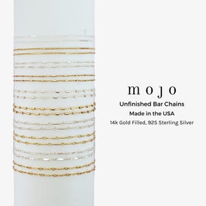 Könnte beinhalten: Eine Auswahl an filigranen Barrenketten in Gold- und Silberfarben. Die Ketten werden auf einer weißen zylindrischen Form präsentiert. Das Bild enthält den Text "mojo", "Unfinished Bar Chains", "Made in the USA" und "14k Gold Filled, 925 Sterling Silver."