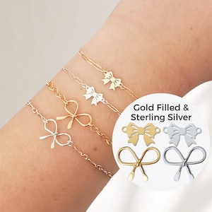May include: A woman's wrist wearing four delicate gold and silver chain bracelets with bow charms. The image also shows close-up views of the bow charms in gold filled and sterling silver.