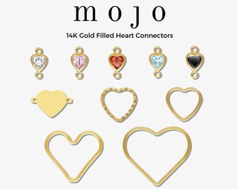 May include: A collection of 14K gold-filled heart connectors. The image displays various heart-shaped charms, some with gemstones in clear, pink, red, and blue. Other charms are plain gold, with one having a textured design. The word "mojo" is at the top.
