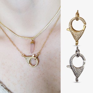 Op de afbeelding: Gouden en zilverkleurige kettinggespen met een pavé diamant ontwerp. De gespen worden getoond op een witte achtergrond.