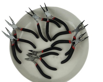 Puede incluir: Un juego de ocho alicates de mango negro con detalles rojos en un plato blanco. Los alicates se utilizan para la elaboración de joyas.