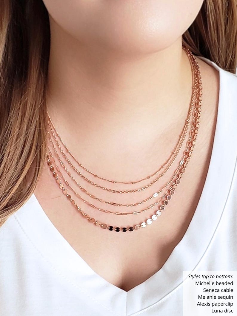 Puede incluir: Un conjunto de collares superpuestos con cinco estilos de cadena diferentes, que incluyen una cadena de cuentas, una cadena de cable, una cadena de lentejuelas, una cadena de clip de papel y una cadena de disco. Las cadenas son todas de color oro rosa.