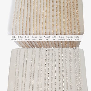 May include: A display of gold-filled and sterling silver chains in various styles, including dainty, link, flat bar, cable, oval, bar, paperclip, hearts, and circle. The chains are arranged in two rows on a white surface. The text "Shop our Gold Filled and Sterling Silver Chains Premium Quality, Made in the USA" is at the top of the image.
