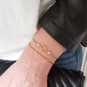 May include: Two gold bracelets with small clear stones. The top bracelet features a star charm. Shown top to bottom: Celeste paperclip chain, Berkeley connectors, Cait star connector.