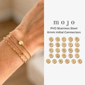 Puede incluir: Pulseras iniciales doradas con una variedad de estilos de cadena se muestran en una muñeca. Las pulseras presentan la letra "T" y están hechas de acero inoxidable PVD con conectores iniciales de 6 mm. Se muestra una tabla de letras.