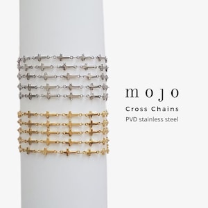 May include: A set of six gold and silver cross chain bracelets. The bracelets are stacked on top of each other and are displayed on a white background. The text "mojo Cross Chains PVD stainless steel" is visible in the image.