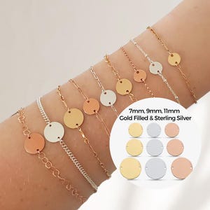 Può includere: Un set di braccialetti delicati in oro pieno e argento sterling con ciondoli rotondi. I ciondoli sono disponibili in tre dimensioni: 7 mm, 9 mm e 11 mm. I braccialetti sono mostrati sul polso di una persona.