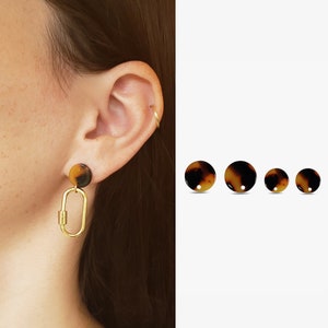 May include: A pair of gold hoop earrings with a brown and black tortoiseshell design. The earrings are shown on a person's ear.