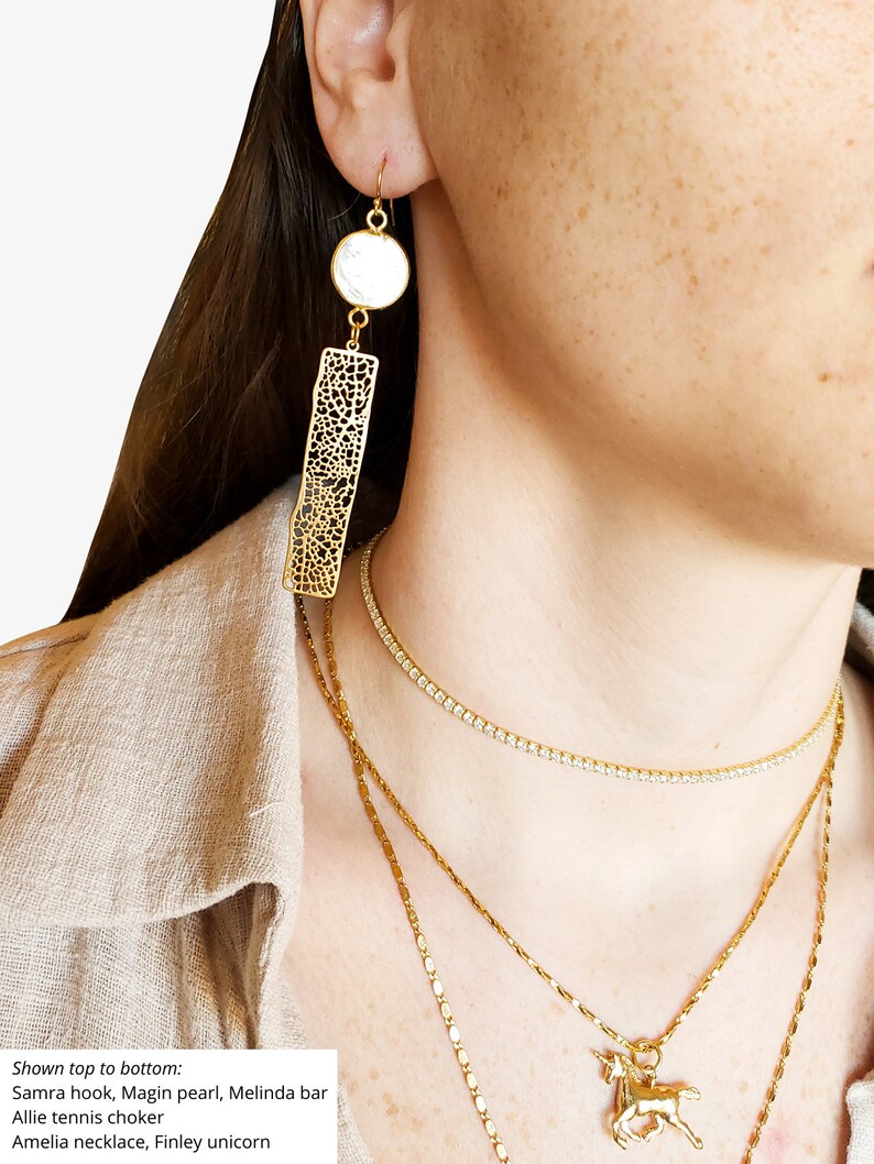 May include: Gold-toned earrings with a white circular accent and a rectangular, openwork design. A gold necklace with a unicorn pendant and other gold necklaces are also visible. The image shows jewelry.