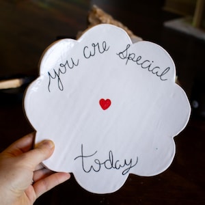 May include: White, cloud-shaped decorative plate with the words "You are Special Today" in black script. A small red heart is centered on the plate. The plate is held by a hand.