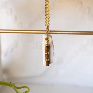 May include: A gold chain necklace featuring a pendant composed of a vertical white stone piece accented with two small brown cylindrical beads separated and capped by three tiny gold-toned metal rings, suspended from a gold jump ring.
