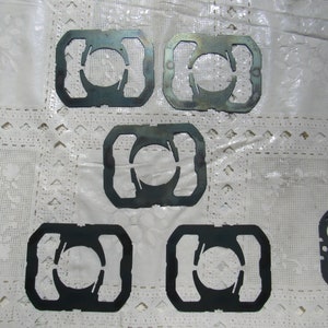 May include: Eight metal cutouts in the shape of a circle with a curved line through it. The cutouts are arranged in a pattern on a white surface.