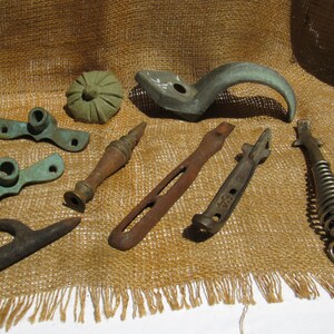 May include: A collection of antique metal hardware pieces in various shapes and sizes. Includes a curved handle, a decorative knob, and several pieces with holes and brackets. The items display a range of colors, from aged bronze to rusty brown.