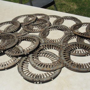May include: A collection of circular, metal objects with a rusty brown color. Each object has a series of evenly spaced slots around the perimeter and a central opening. The objects are arranged on a light-colored surface.