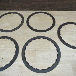 May include: Five black metal clutch plates for a motorcycle or other vehicle. The plates are circular and have a serrated edge.