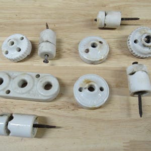 May include: Assortment of vintage porcelain electrical insulators with various shapes and sizes. Some insulators have a nail or screw protruding from the bottom.