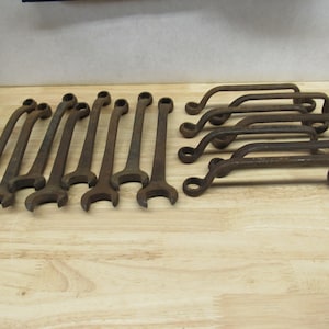 May include: A collection of 15 rusty wrenches, some with curved handles, arranged on a wooden surface.