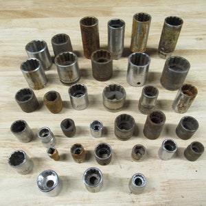 May include: A collection of vintage socket wrenches in various sizes, some with chrome plating and others with rust. The sockets are arranged on a wooden surface.