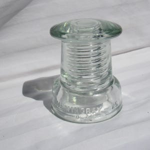 May include: A clear glass insulator with a ribbed design and the text "Hemingray 25" on the bottom.