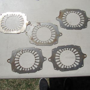 May include: Five metal plates with a circular design and a central hole. The plates have a silver color with some rust spots. The plates are arranged on a light-colored surface.