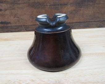 Op de afbeelding: Een bruine keramische isolator met een zwarte bovenkant en witte accenten. De isolator heeft een belvorm en is ontworpen voor elektrische bedrading.