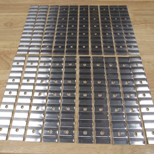 May include: A set of 48 silver metal strips with holes and a wavy texture. The strips are arranged in rows on a wooden surface.