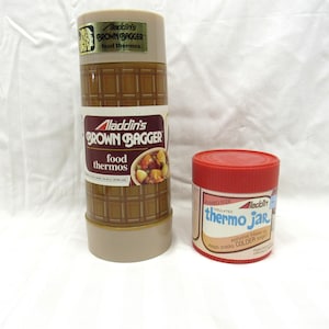 May include: Two vintage Aladdin food thermoses. A brown and gold checkered food thermos with the text "Aladdin's Brown Bagger food thermos". A red insulated thermo jar with the text "Aladdin thermo jar insulated cooler longer".